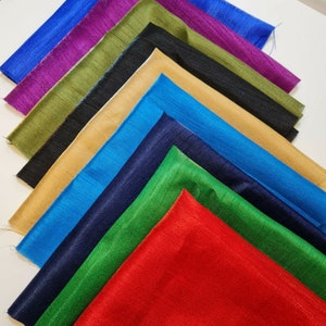 Può includere: Una collezione di dieci campioni di tessuto in vari colori, tra cui rosso, verde, blu, oro e viola. I campioni sono disposti a ventaglio, con il campione rosso in basso e il campione viola in alto.