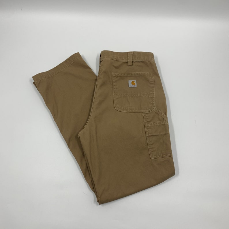 Puede incluir: Pantalones de trabajo color caqui con m&uacute;ltiples bolsillos y un peque&ntilde;o parche con el logotipo en la parte trasera. Los pantalones est&aacute;n hechos de un material duradero y est&aacute;n dise&ntilde;ados para el trabajo o el uso informal.