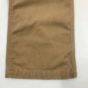 Puede incluir: Primer plano de la parte inferior de un pantal&oacute;n color caqui. La tela es de color beige liso con costuras visibles a lo largo de las costuras y el dobladillo. El pantal&oacute;n parece estar hecho de un material duradero.