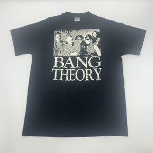 Könnte beinhalten: Schwarzes T-Shirt mit einem weißen Aufdruck einer Personengruppe und dem Text "BANG THEORY". Das Shirt hat kurze Ärmel und besteht aus einem weichen Material. Das Design ist im Vintage-Stil.