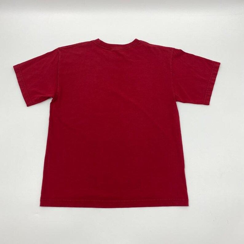Puede incluir: Una camiseta roja lisa de manga corta y cuello redondo. La parte trasera de la camiseta es visible, mostrando el dise&ntilde;o sencillo. La camiseta est&aacute; hecha de un material suave. Esta camiseta informal es adecuada para el uso diario.