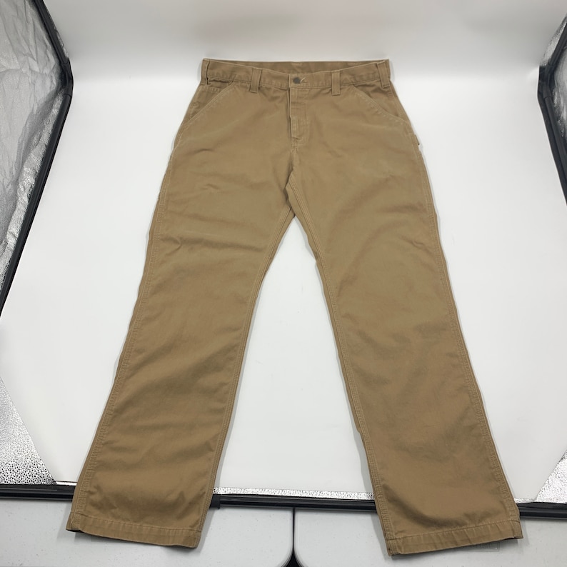 Puede incluir: Pantalones de trabajo color caqui con cierre de bot&oacute;n y trabillas para el cintur&oacute;n. Los pantalones tienen un dise&ntilde;o cl&aacute;sico de cinco bolsillos y una pernera recta. La tela parece ser una mezcla de algod&oacute;n duradera, adecuada para el trabajo o el uso informal.