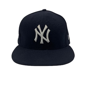 May include: A navy blue baseball cap with a white embroidered "NY" logo on the front. The cap has a structured crown and a curved brim. The New Era logo is visible on the side.