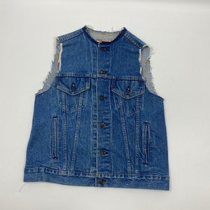 Op de afbeelding: Een blauw spijkergoed vest met een knoopsluiting, twee borstzakken en twee zijzakken. Het vest heeft een distressed, rafelig ontwerp op de schouders en kraag. Het merk Levi's is zichtbaar.