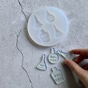 May include: A silicone mould with four different bottle shapes. The mould is white and has the following text on the bottles: 2D4 + 2HP, 4D4 + 4HP, 8D4 + 8HP, 10D4 + 20HP. There are also four clear resin bottles with the same text on them.
