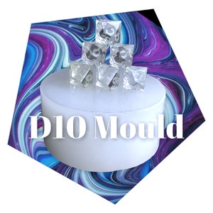 May include: A white silicone mold for making D10 dice. The mold is sitting on a table with a swirling blue, purple, and white background. Six clear D10 dice are stacked on top of the mold.