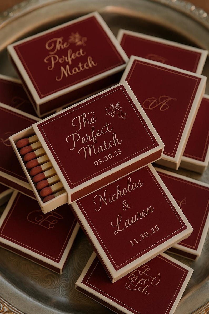 May include: Burgundy matchboxes with ivory trim are arranged on a silver tray. The boxes feature the text "The Perfect Match" and dates, with one box open, revealing the matches. Other boxes have names and dates.