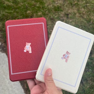 May include: Two red and white book covers with a teddy bear design. The teddy bear is wearing a blue bow tie. The covers are made of a textured material.