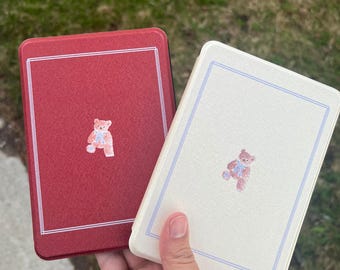 May include: Two book covers in red and white with a teddy bear design. The teddy bear is wearing a blue bow tie. The covers are made of a textured material.
