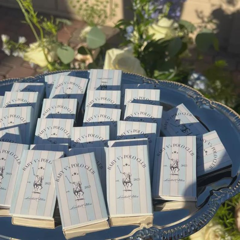 May include: A collection of matchboxes arranged on a silver tray. Each matchbox features a light blue and white striped design with the text "BABY V'S POLO CLUB" and a polo player logo. The words "Limited Edition" are also visible.
