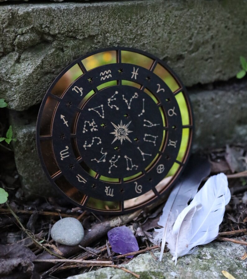 K&ouml;nnte beinhalten: Ein h&ouml;lzernes Zodiakrad mit schwarzem Hintergrund und goldenen Akzenten. Das Rad zeigt die zw&ouml;lf Tierkreiszeichen und Sternbilder. Das Rad ist von einem goldenen Ring umgeben.