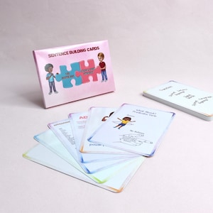May include: A pink box with the words "Sentence Building Cards" and an illustration of two children holding puzzle pieces. The box contains a set of colorful cards with words and illustrations.
