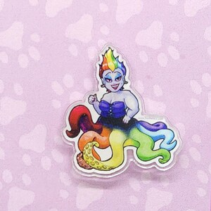 Op de afbeelding: Een regenboogkleurige octopus met een vrouw met paars haar die erop zit. De vrouw draagt een paarse top en een zwarte rok. De octopus heeft een gele en oranje ring om zijn kop. De achtergrond is een roze en wit pootprintpatroon. De tekst "www.NicDaStick.com" staat onderaan de afbeelding.