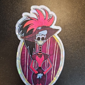 May include: A sticker featuring a cartoon character with a large, red and black feathered hat, a black and white striped dress, and a red and black umbrella. The character has a wide smile and is standing in front of a purple and white striped background.