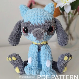 Peut inclure: Peluche crochetée en forme de créature bleue et grise avec de grands yeux noirs. La peluche a des accents jaunes sur les pieds et le cou. Le texte "PDF PATTERN ONLY" est visible sur l'image.