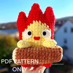 May include: Crochet pattern for a fire spirit amigurumi toy. The toy is red, yellow, and brown and is sitting on a log. The pattern is available as a PDF download. @songbirdcrochetart