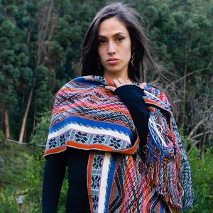 May include: A woman wearing a black long-sleeved shirt and a colourful woven shawl with fringe. The shawl has a geometric pattern in shades of red, orange, blue, and white.