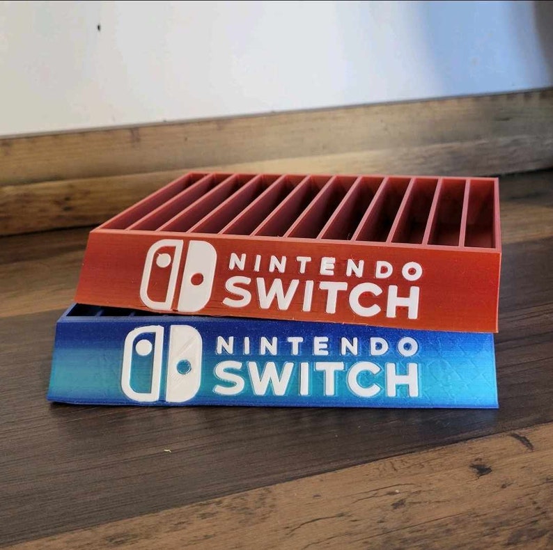 May include: Two Nintendo Switch game cartridge holders. The top holder is red, and the bottom holder is blue with a gradient effect. Both holders have the Nintendo Switch logo and text in white.