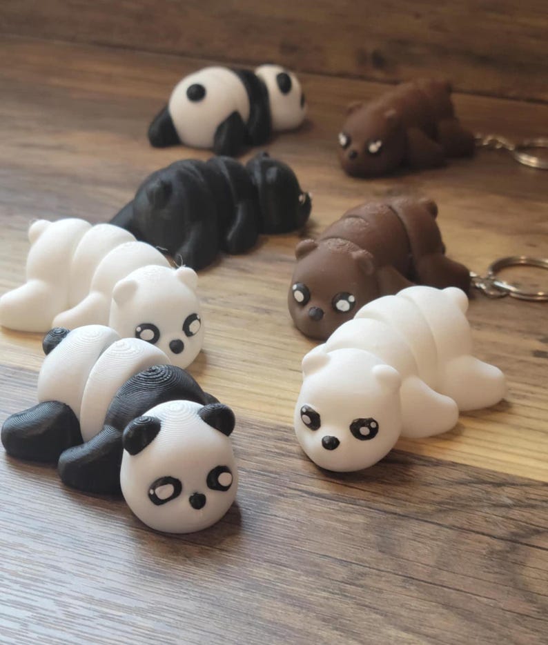 K&ouml;nnte beinhalten: Ein Set mit sechs 3D-gedruckten B&auml;ren-Schl&uuml;sselanh&auml;ngern. Die Schl&uuml;sselanh&auml;nger sind in verschiedenen Farben, darunter Schwarz, Wei&szlig; und Braun. Jeder Schl&uuml;sselanh&auml;nger zeigt einen B&auml;ren in Schlafposition mit einem niedlichen, cartoonartigen Gesicht.