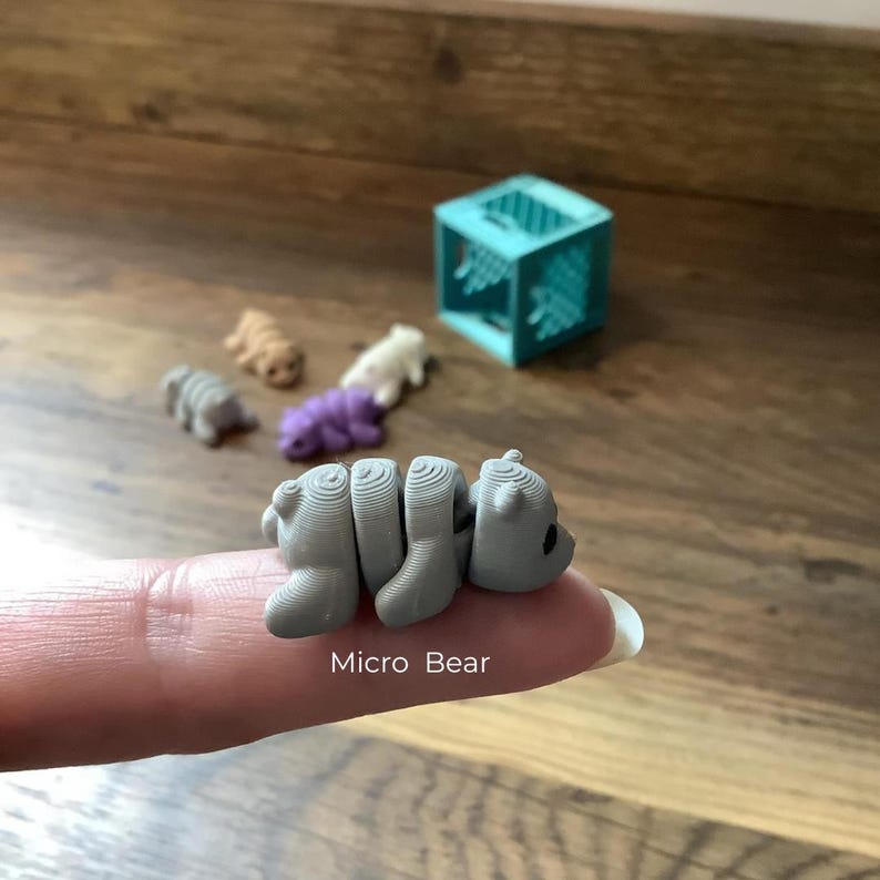 K&ouml;nnte beinhalten: Eine kleine graue 3D-gedruckte B&auml;renfigur, die sich in Schlafposition zusammengerollt hat. Der B&auml;r ist etwa so gro&szlig; wie eine Fingerspitze und hat eine strukturierte Oberfl&auml;che. Der Text "Micro Bear" steht unter dem B&auml;ren.