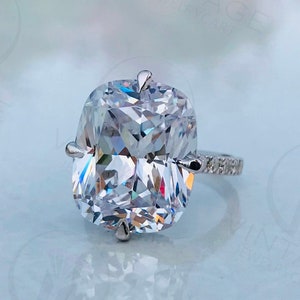 May include: A silver ring with a large, clear, cushion-cut gemstone. The ring has a thin band with small, clear gemstones.