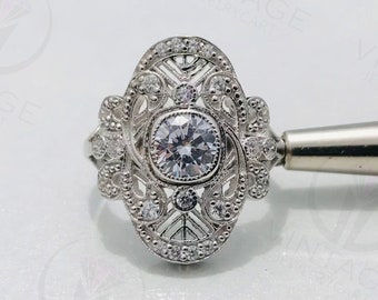 May include: A silver ring with a large, round, clear gemstone surrounded by smaller, clear gemstones. The ring has a delicate, intricate design.