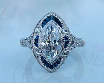 May include: A marquise cut diamond engagement ring with a halo of smaller diamonds and a band of blue sapphires.