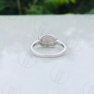 May include: A silver ring with a pear-shaped diamond surrounded by smaller diamonds. The ring is set with a pave setting and has a polished finish.