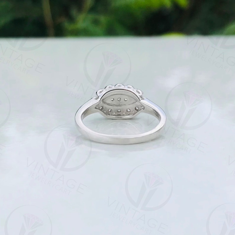 May include: A silver ring with a pear-shaped diamond surrounded by smaller diamonds. The ring is set with a pave setting and has a polished finish.
