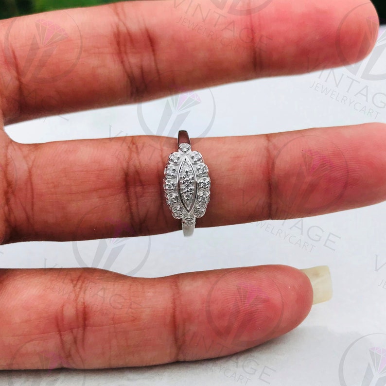 May include: A silver ring with a row of small diamonds set in a leaf-shaped design. The ring is on a finger.