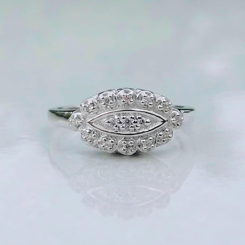 May include: A silver ring with a diamond-shaped center stone surrounded by smaller diamonds. The ring has a unique design with a scalloped edge.