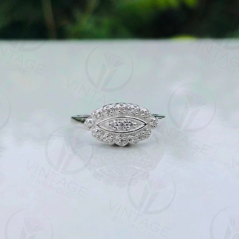 May include: A silver ring with a row of small diamonds set in an oval shape. The ring has a delicate design and is perfect for everyday wear.