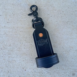 May include: A black leather keychain featuring a matte black metal swivel lobster clasp at the top. The leather strap has a rounded bottom, a single copper-colored rivet, and a debossed logo. A circular leather loop is attached at the base.