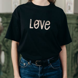 Pu&ograve; includere: Una maglietta nera con la parola "Love" scritta in color marrone chiaro sul davanti.