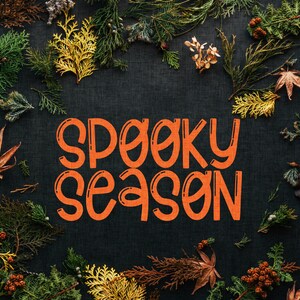 Pu&ograve; includere: Uno sfondo scuro con foglie autunnali che circondano il testo "Spooky Season" in arancione.
