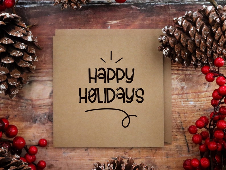 Pu&ograve; includere: Un biglietto marrone con il testo "Happy Holidays" scritto in nero. Il biglietto &egrave; circondato da pigne e bacche rosse.