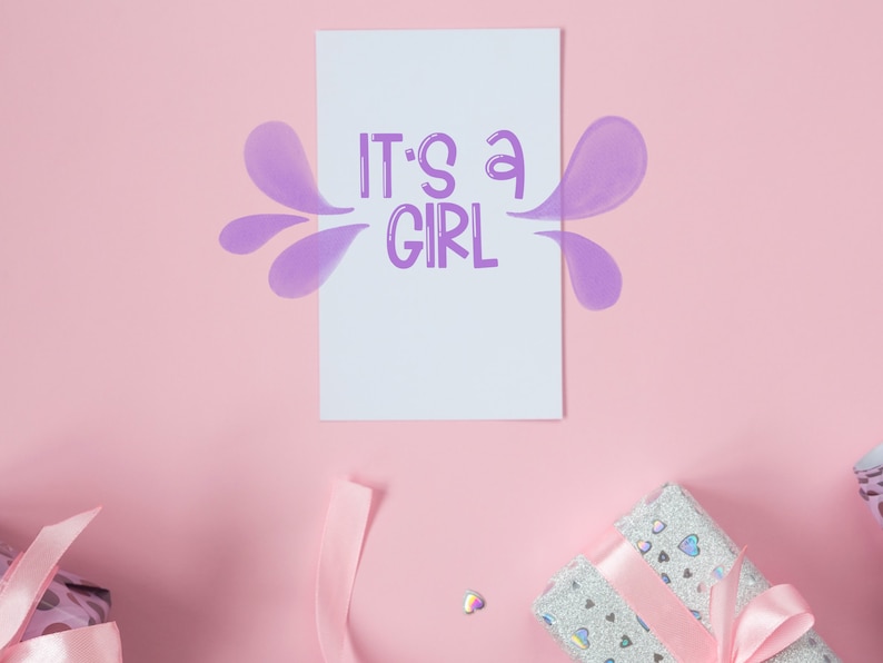 Pu&ograve; includere: Un biglietto rosa con il testo "It's a girl" in lettere viola. Il biglietto &egrave; circondato da forme viola simili ad acquerello. Due scatole regalo con nastro rosa sono sullo sfondo rosa.