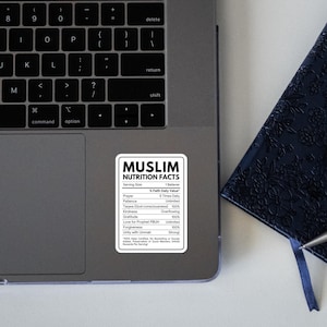 May include: A silver laptop with a rectangular sticker featuring a black and white nutrition facts label titled MUSLIM NUTRITION FACTS, listing values for prayer, patience, kindness, and forgiveness, placed next to a dark blue textured notebook and pen.