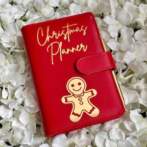 Puede incluir: Planificador de Navidad de cuero rojo con un dise&ntilde;o de hombre de jengibre dorado y el texto "Christmas Planner" en letras doradas.
