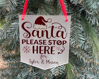 May include: White frosted sign with red text that reads "Santa Please Stop Here for Tyler & Mason". The sign has a red ribbon attached to the top and a red Santa hat graphic.