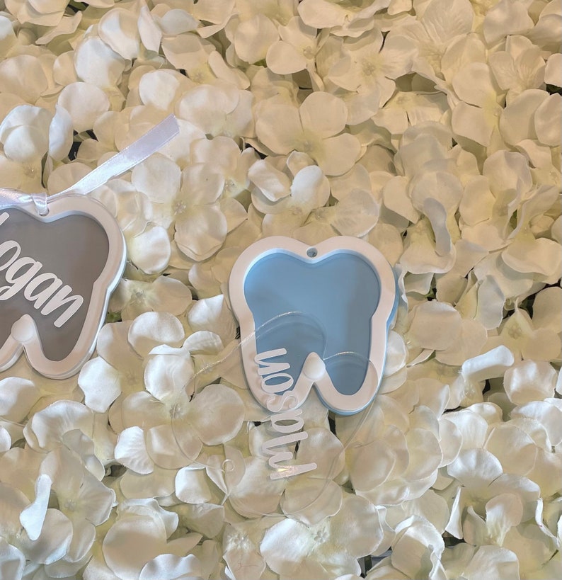 May include: Two white tooth-shaped ornaments with the names "Logan" and "Mason" written on them. The ornaments are on a white background.