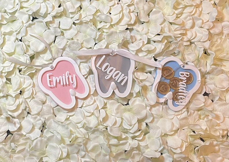 May include: A tooth-shaped banner with three sections, each with a different name. The first section is pink and says "Emily", the second is gray and says "Logan", and the third is blue and says "Bradley".