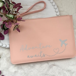 May include: A pink zippered pouch with a silver airplane and heart design and the text "Adventure awaits".