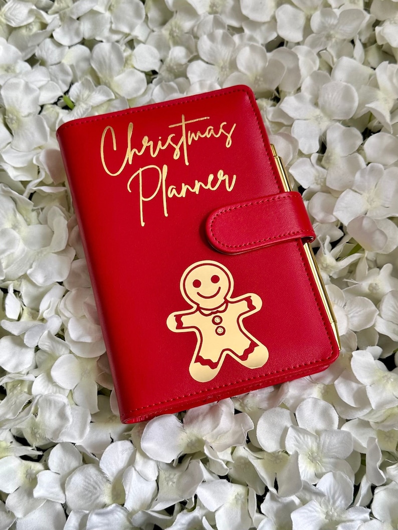 Puede incluir: Planificador de Navidad de cuero rojo con un dise&ntilde;o de hombre de jengibre dorado y el texto "Christmas Planner" en letras doradas.