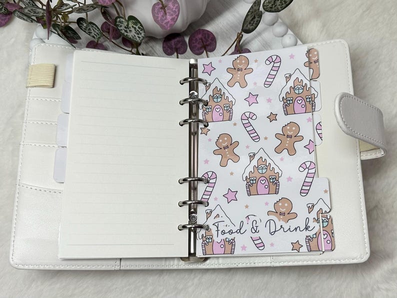 May include: A white planner with a gingerbread house and candy cane pattern on the tab dividers. The tab dividers are labeled "Food & Drink".