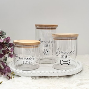May include: Three clear glass jars with bamboo lids. The jars are labelled "Bonnie's Treats" with a paw print, bone, and paw print designs.