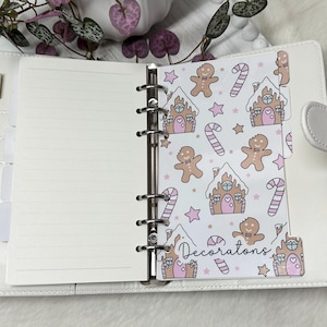 May include: A white planner with a gingerbread house and candy cane pattern on the tab. The tab says "Decorations".