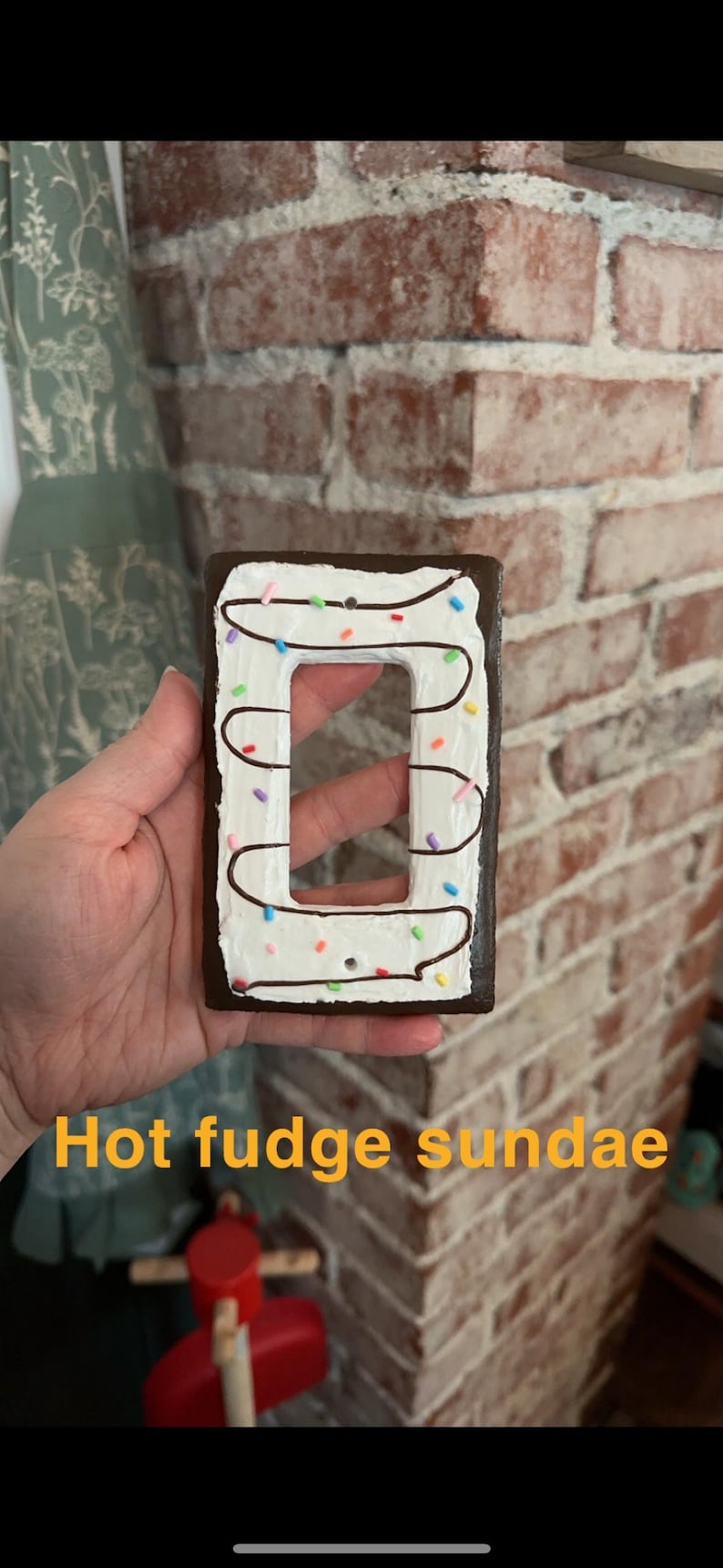 K&ouml;nnte beinhalten: Ein Lichtschalter-Abdeckung, die wie ein hei&szlig;er Schokoladen-Sundae bemalt ist. Die Abdeckung ist braun mit wei&szlig;em Frosting und bunten Streuseln.