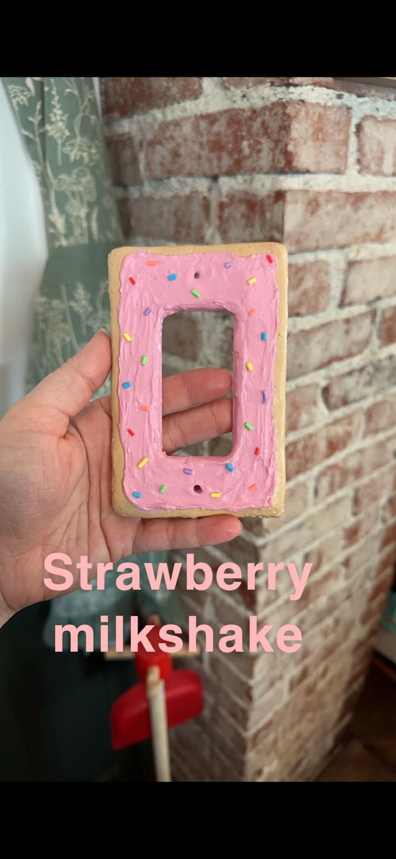 K&ouml;nnte beinhalten: Ein Lichtschalter-Abdeckung in Form eines glasierten Donuts mit rosa Zuckerguss und bunten Streuseln. Der Text "Strawberry milkshake" steht unter dem Donut.