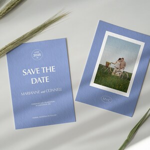 May include: A blue save the date card with white text that reads "Save the Date" and "Marianne and Connell". The card also includes the date "June 14, 2025" and the text "Ceremony and Celebration in Camocilla, ME". A second card features a photo of a couple riding a bicycle in a field.